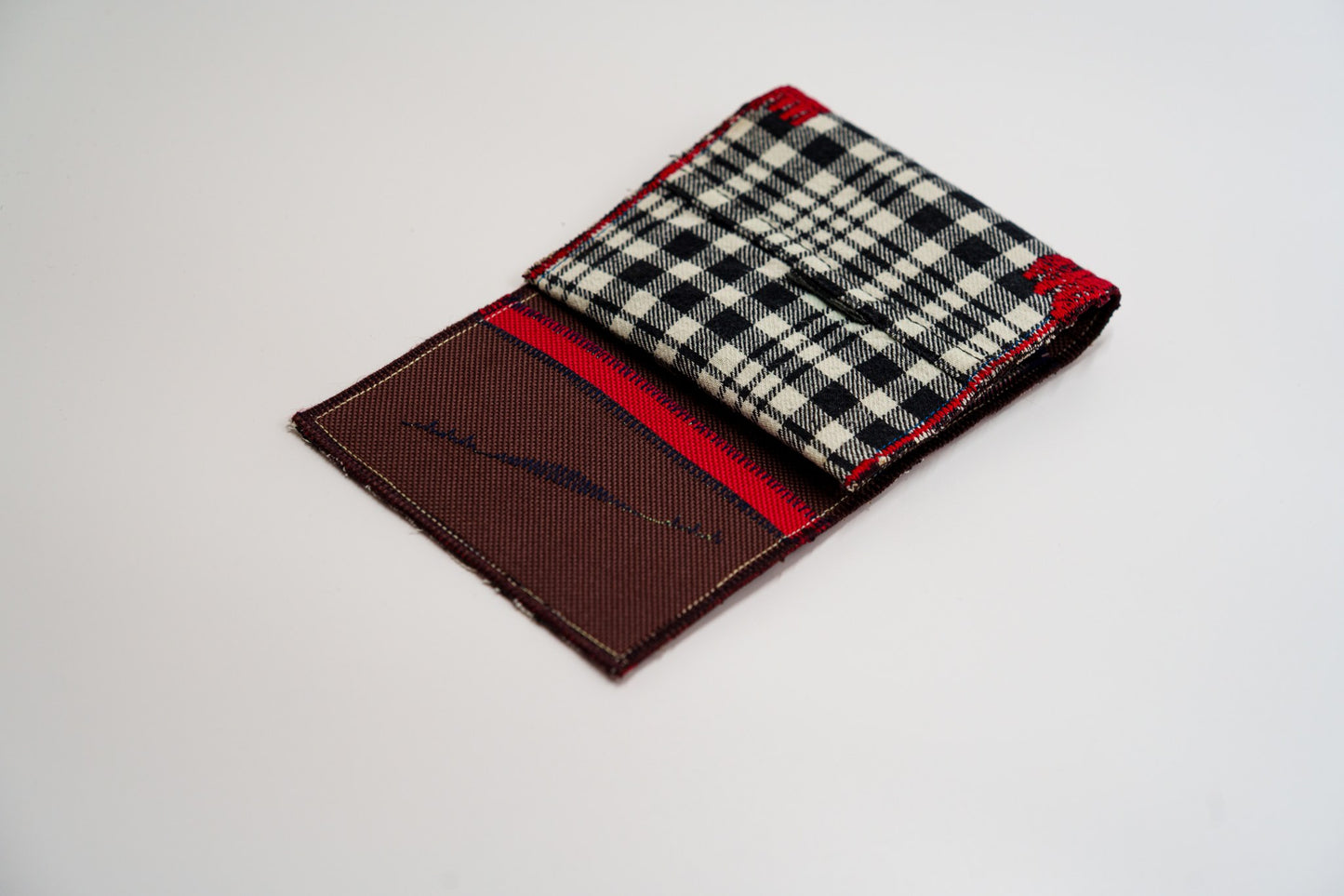 Half-open wallet, warm brown and red interior meeting the black and pale-olive plaid — HighSew