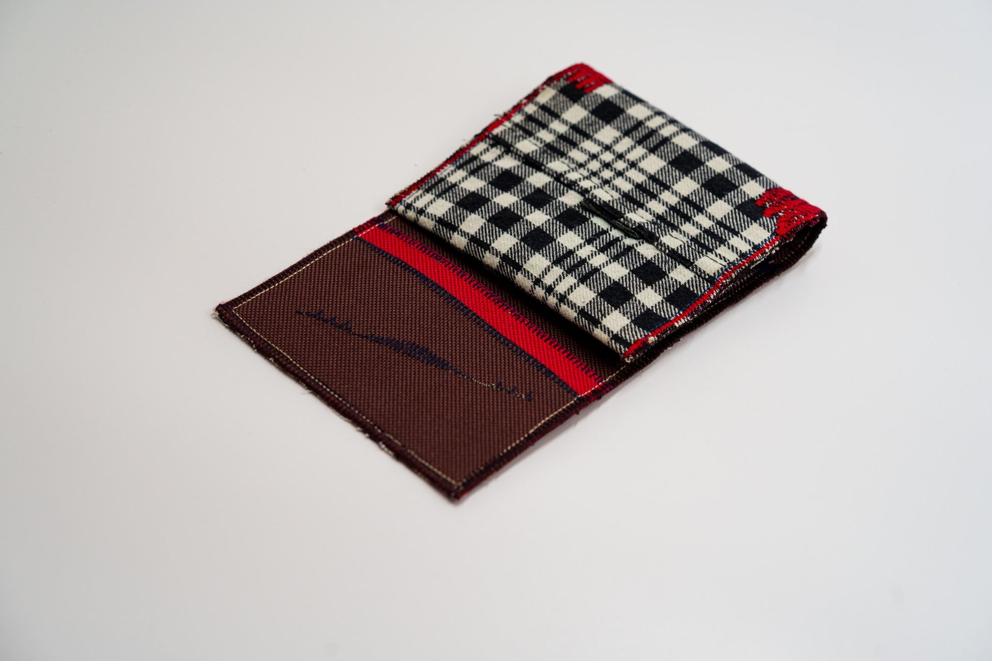 Half-open wallet, warm brown and red interior meeting the black and pale-olive plaid — HighSew