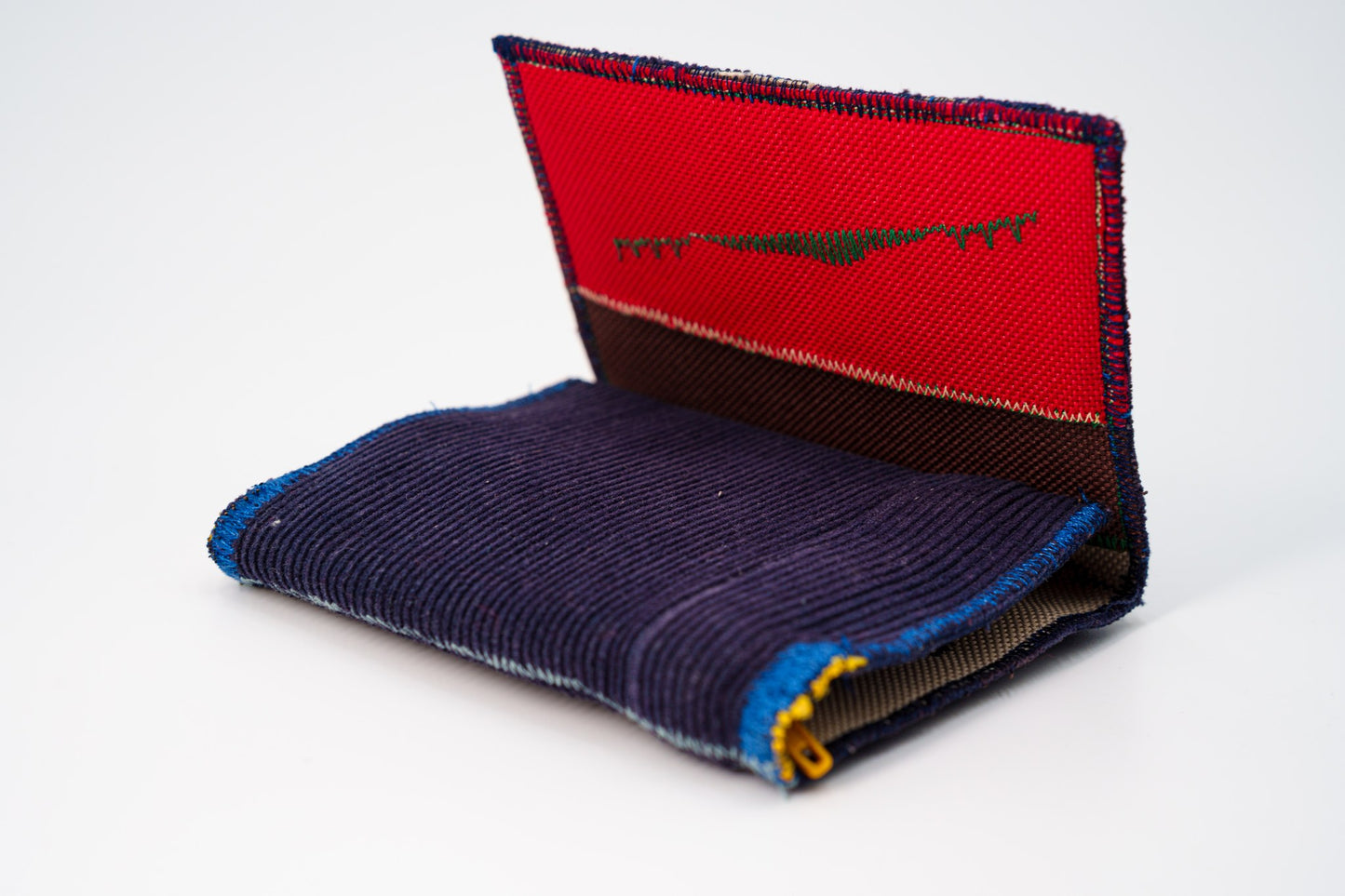 Blue corduroy wallet half-open, red interior panel meeting the deep blue exterior — HighSew