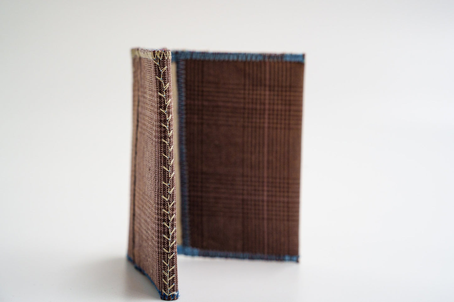 Upcycled wallet standing open, showing cream decorative spine stitching — HighSew