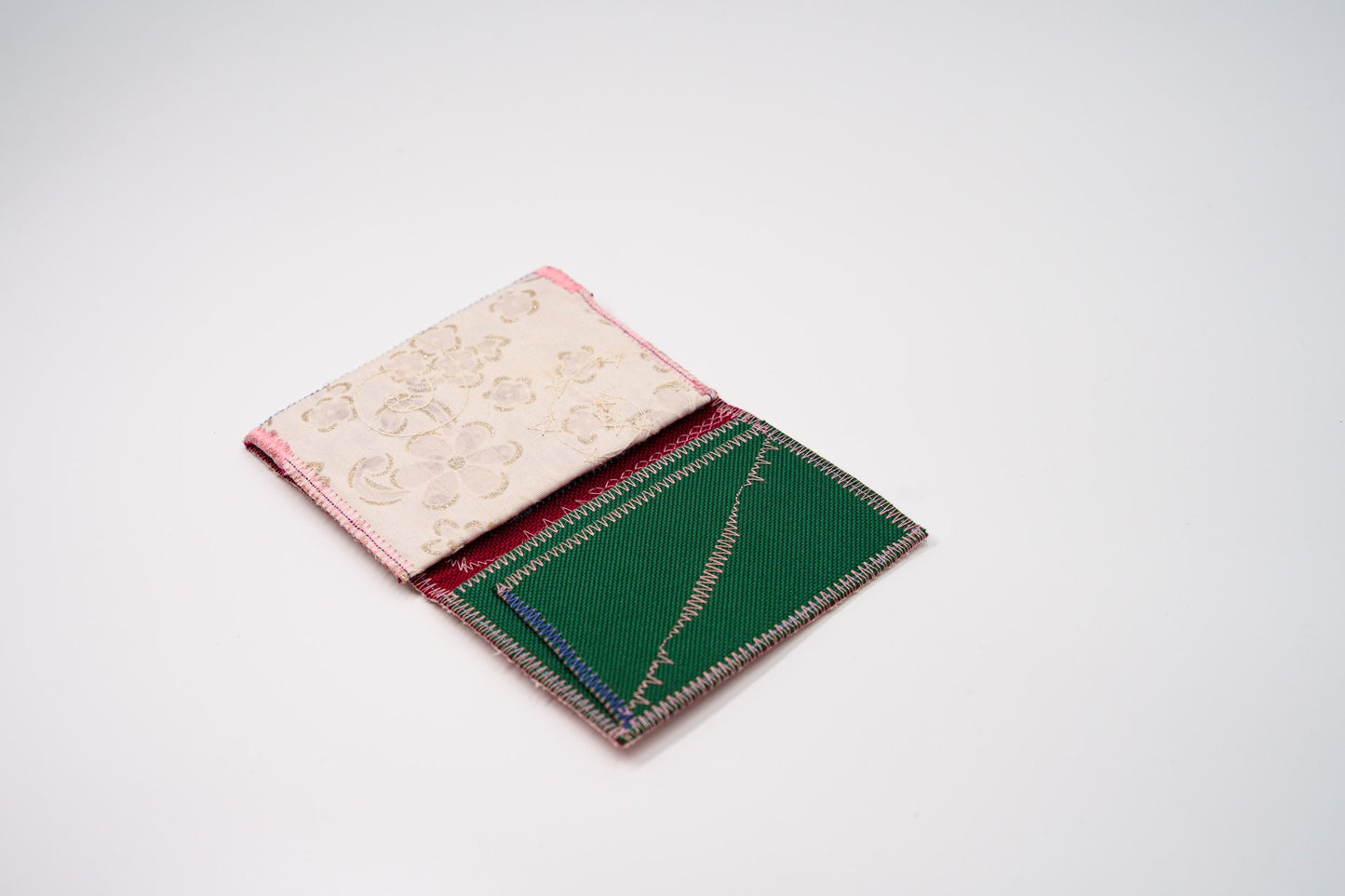 Upcycled wallet open at an angle showing green interior and cream floral exterior — HighSew