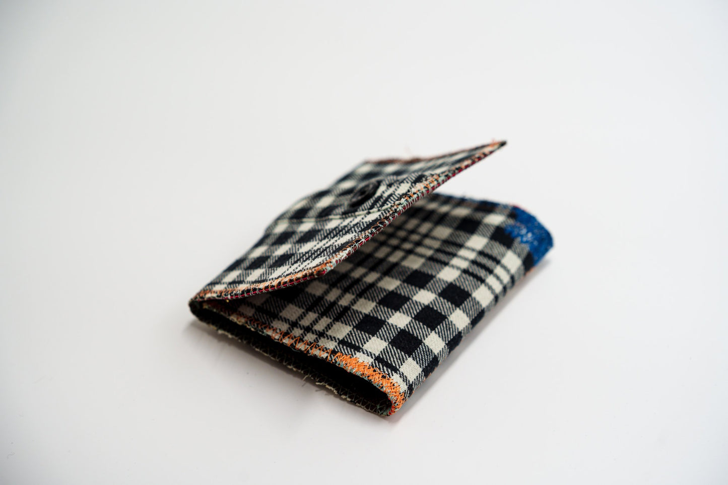 Black and pale-olive plaid flannel wallet, folded closed at an angle, with colorful zigzag edge stitching