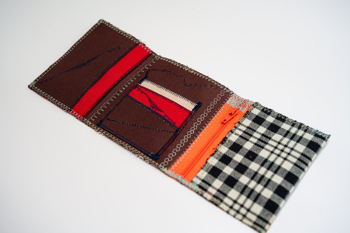 Wallet open flat, top-down: brown and deep-red interior panels with a bright orange zip and card slots
