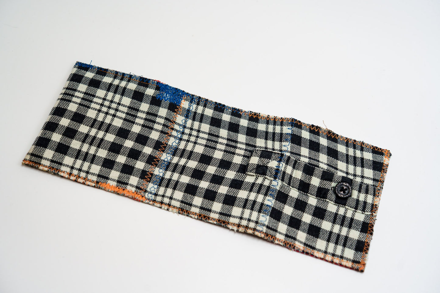 Plaid flannel wallet exterior laid flat, with a small buttoned sleeve pocket and orange edge stitching