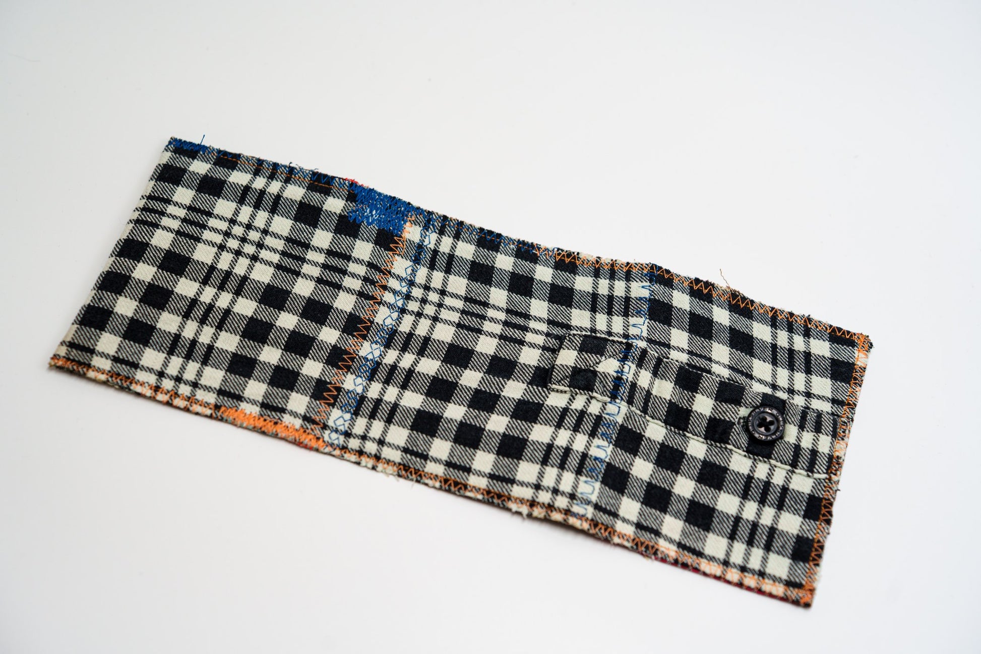 Plaid flannel wallet exterior laid flat, with a small buttoned sleeve pocket and orange edge stitching