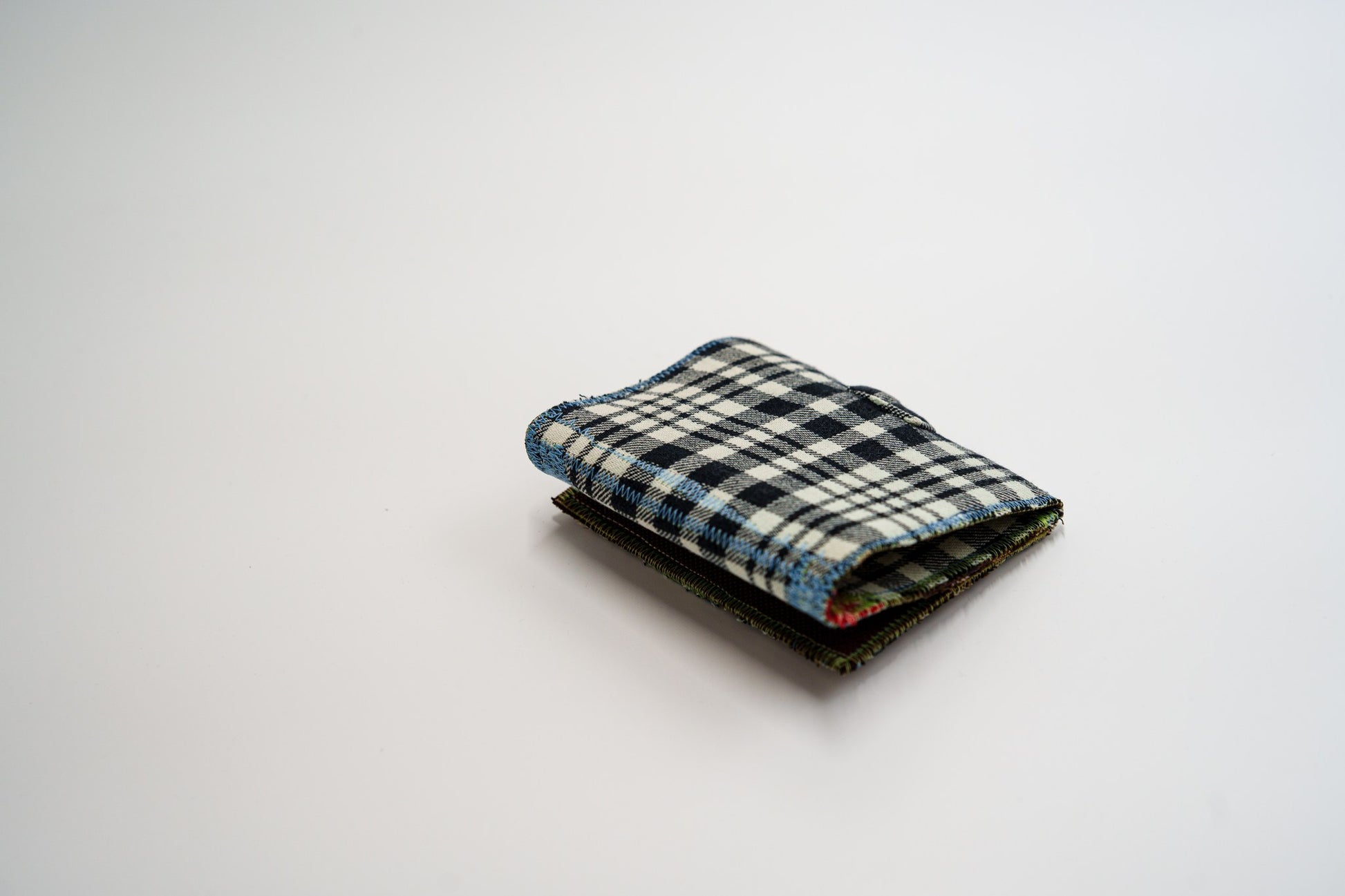 Black and pale-olive plaid flannel wallet, folded closed at an angle, with blue zigzag edge stitching