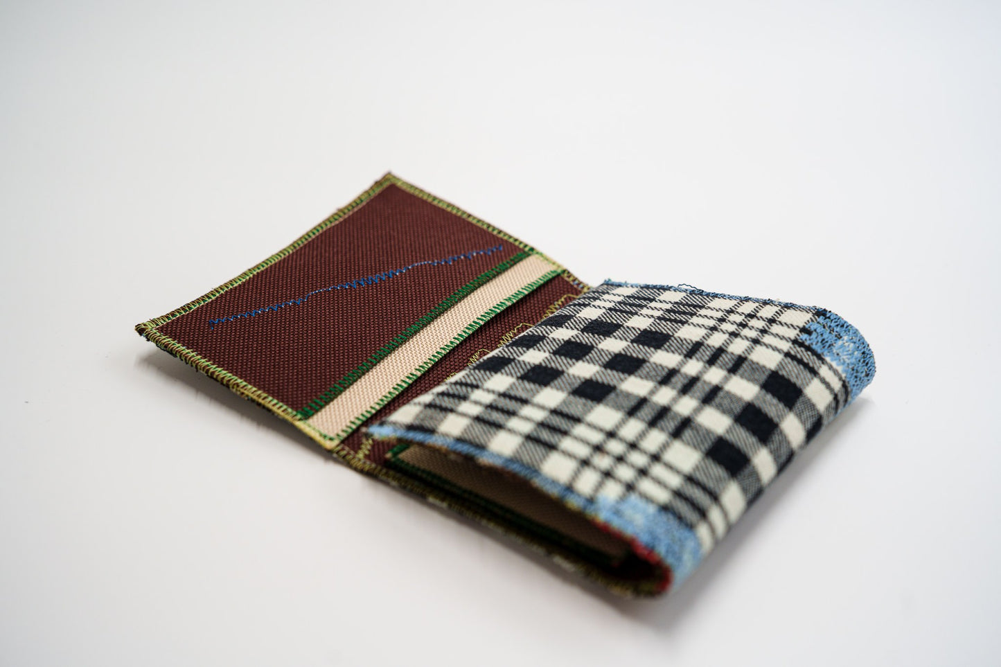 Half-open wallet, black and pale-olive plaid exterior meeting the brown and red interior