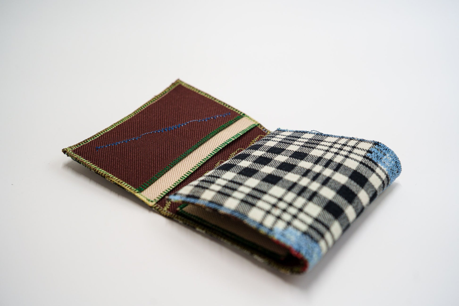 Half-open wallet, black and pale-olive plaid exterior meeting the brown and red interior