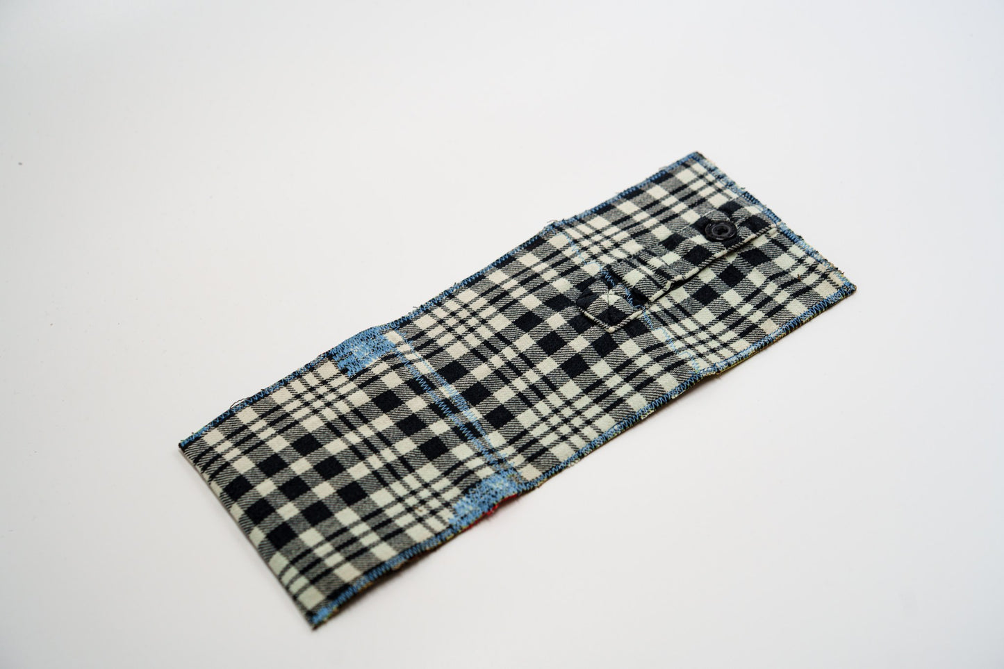 Plaid flannel wallet exterior laid flat, with a small buttoned sleeve pocket and blue edge stitching