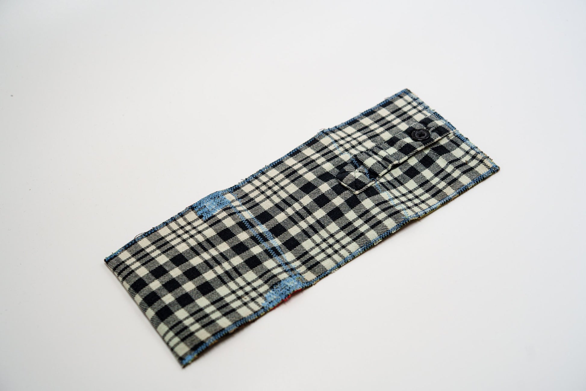 Plaid flannel wallet exterior laid flat, with a small buttoned sleeve pocket and blue edge stitching